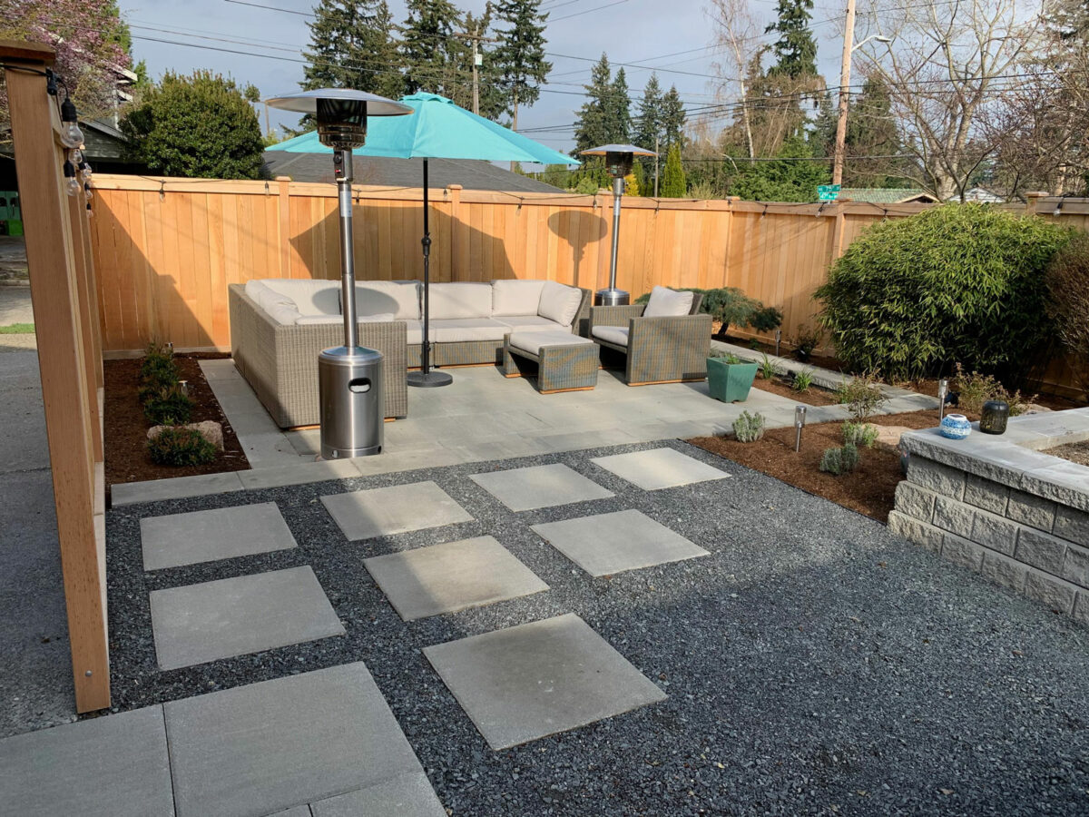 Small residential backyard with rock paver patio and custom garden beds and wood fencing in Seattle, Washington neighborhood.