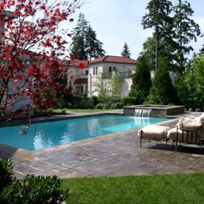 Large blue pool with paver patio has a waterfall feature from the hot tub to the pool at Seattle residence.