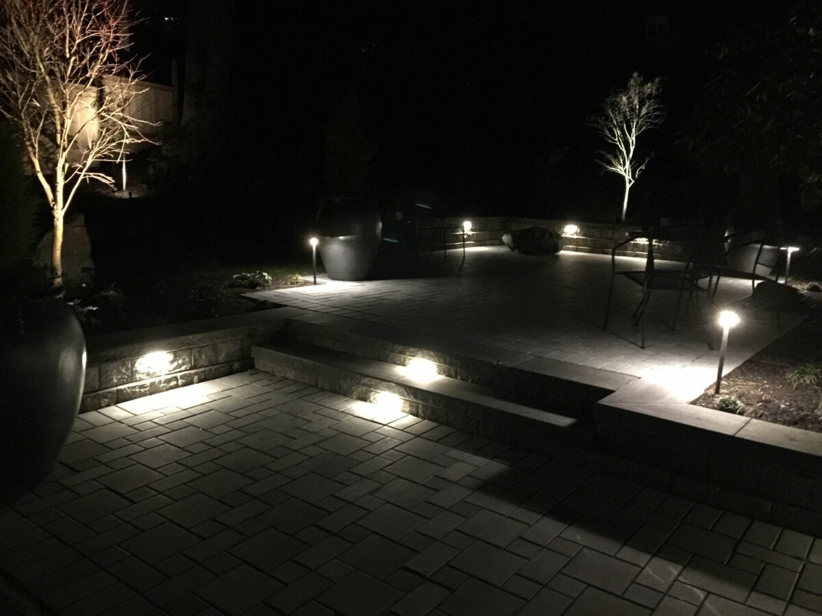 Backyard paver patio seen at night is illuminated with custom outdoor lighting from Bonney Lake Landscapes located in Seattle, Washington.