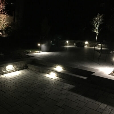 Backyard paver patio seen at night is illuminated with custom outdoor lighting from Bonney Lake Landscapes located in Seattle, Washington.