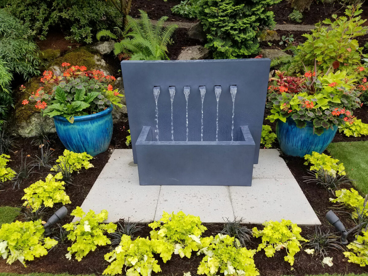 Unique and completely custom rock water fountain with outdoor lighting, paver patio and lush landscape design by Bonney Lake Landscapes in Seattle, Washington.