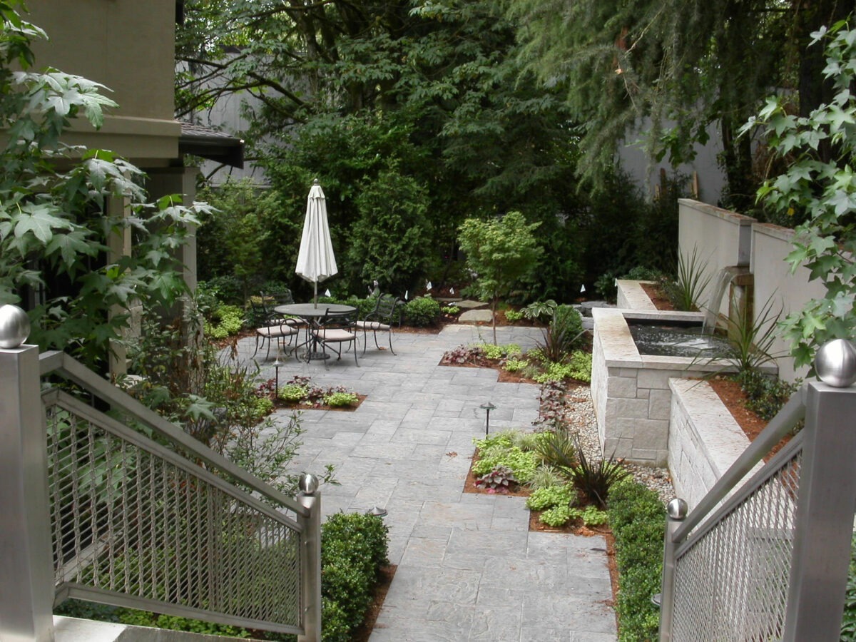 Large Seattle backyard patio with large retaining wall boasts a water fountain and paver patio with luxury landscaping by Bonney Lake Landscapes.