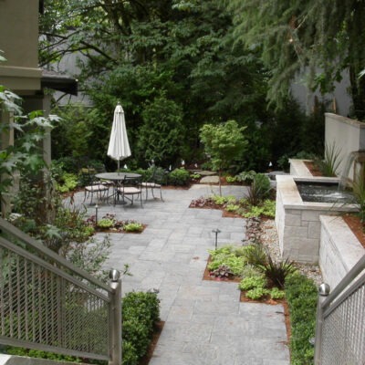 Large Seattle backyard patio with large retaining wall boasts a water fountain and paver patio with luxury landscaping by Bonney Lake Landscapes.